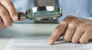 man scrutinizing paperwork with magnifying glass